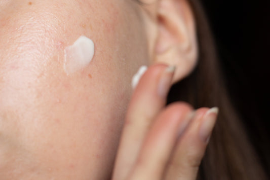 A close up of Caucasian woman swiping a white cream across her cheek 