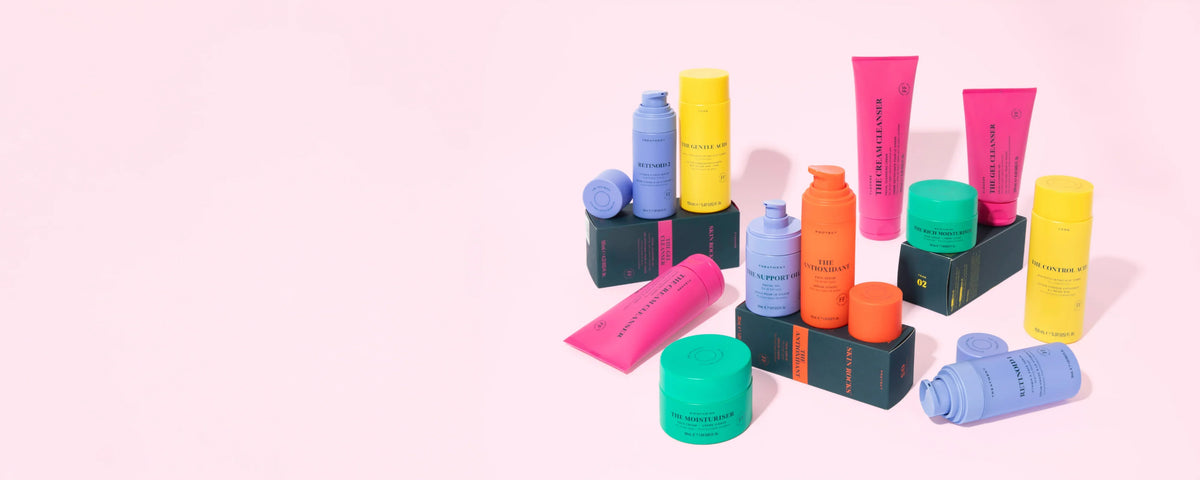 Skin Rocks by Caroline Hirons | Colorful skincare products including cleansers, serums, and moisturizers on pink background