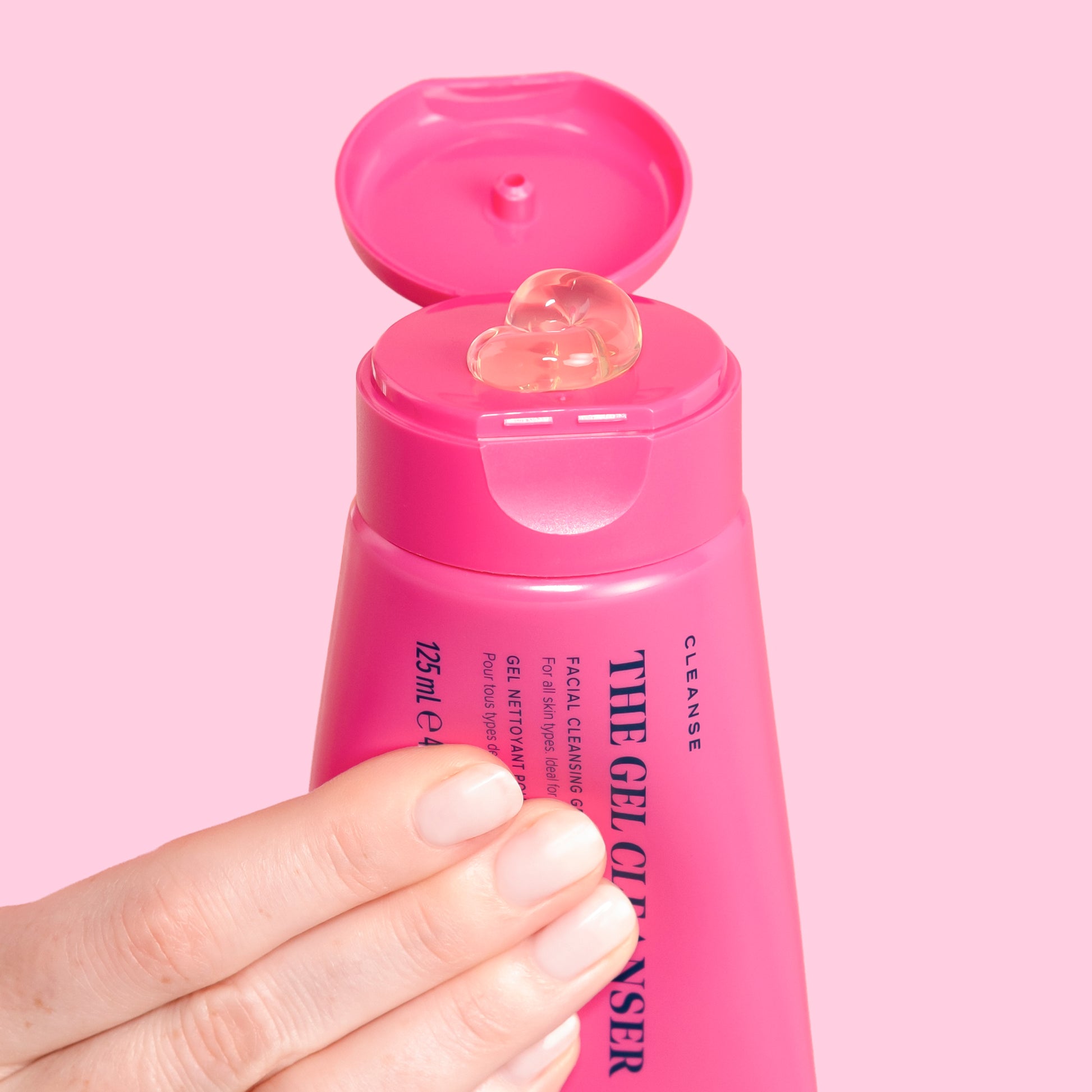 A hand squeezing The Gel Cleanser bottle, against pale pink background | Skin Rocks by Caroline Hirons