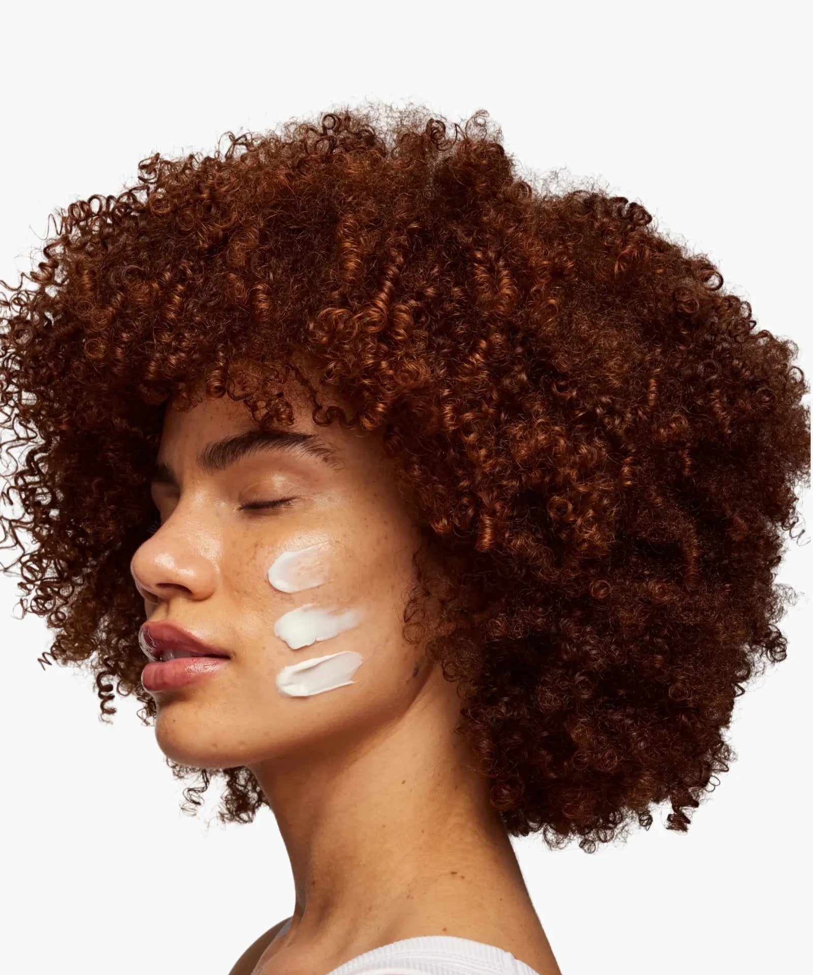 Skin Rocks by Caroline Hirons | Woman applying skincare cream on cheek with curly hair