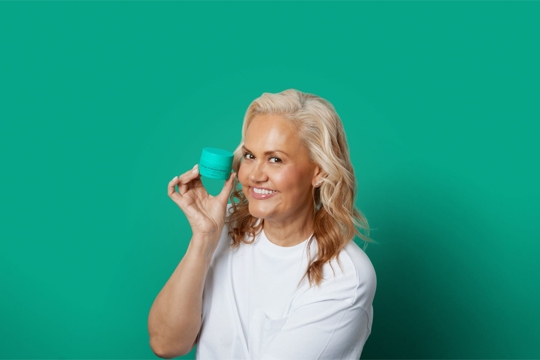 Skin Rocks' Founder, Caroline Hirons holding The Rich Moisturiser against a rich green background