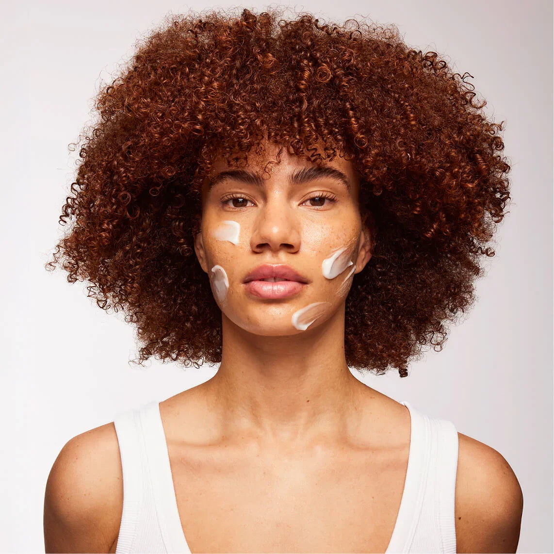 Skin Rocks by Caroline Hirons | Woman applying skincare cream on face with curly hair