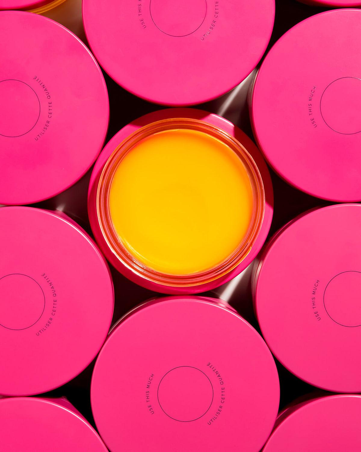 Skin Rocks by Caroline Hirons | Open pink jar showing bright yellow skincare balm surrounded by closed pink jars.